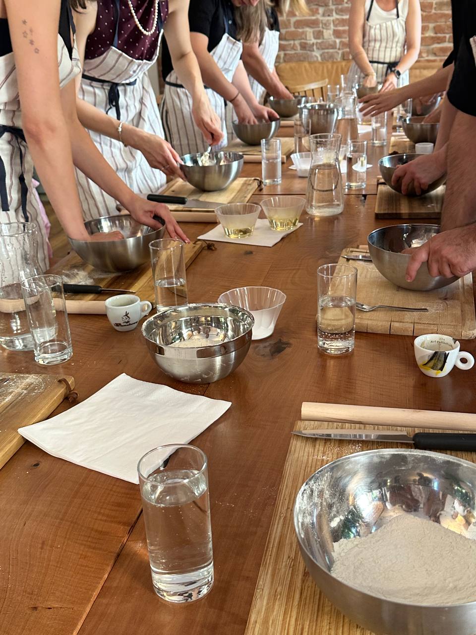 Guests in aprons kneading dough at a long wooden table during a Nomad Küche cooking workshop in Vienna